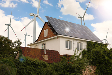 Image of Wind turbines near house with installed solar panels on roof. Alternative energy source