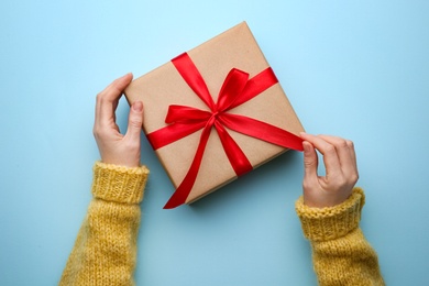 Photo of Woman holding Christmas gift box on light blue background, top view