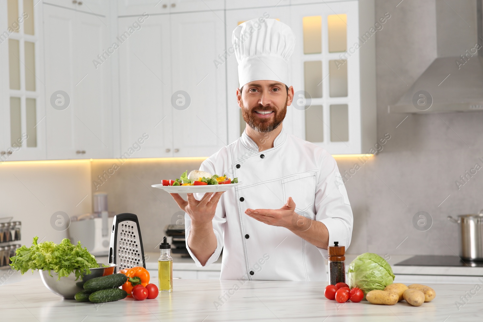 Photo of Professional chef presenting delicious salad at marble table in kitchen