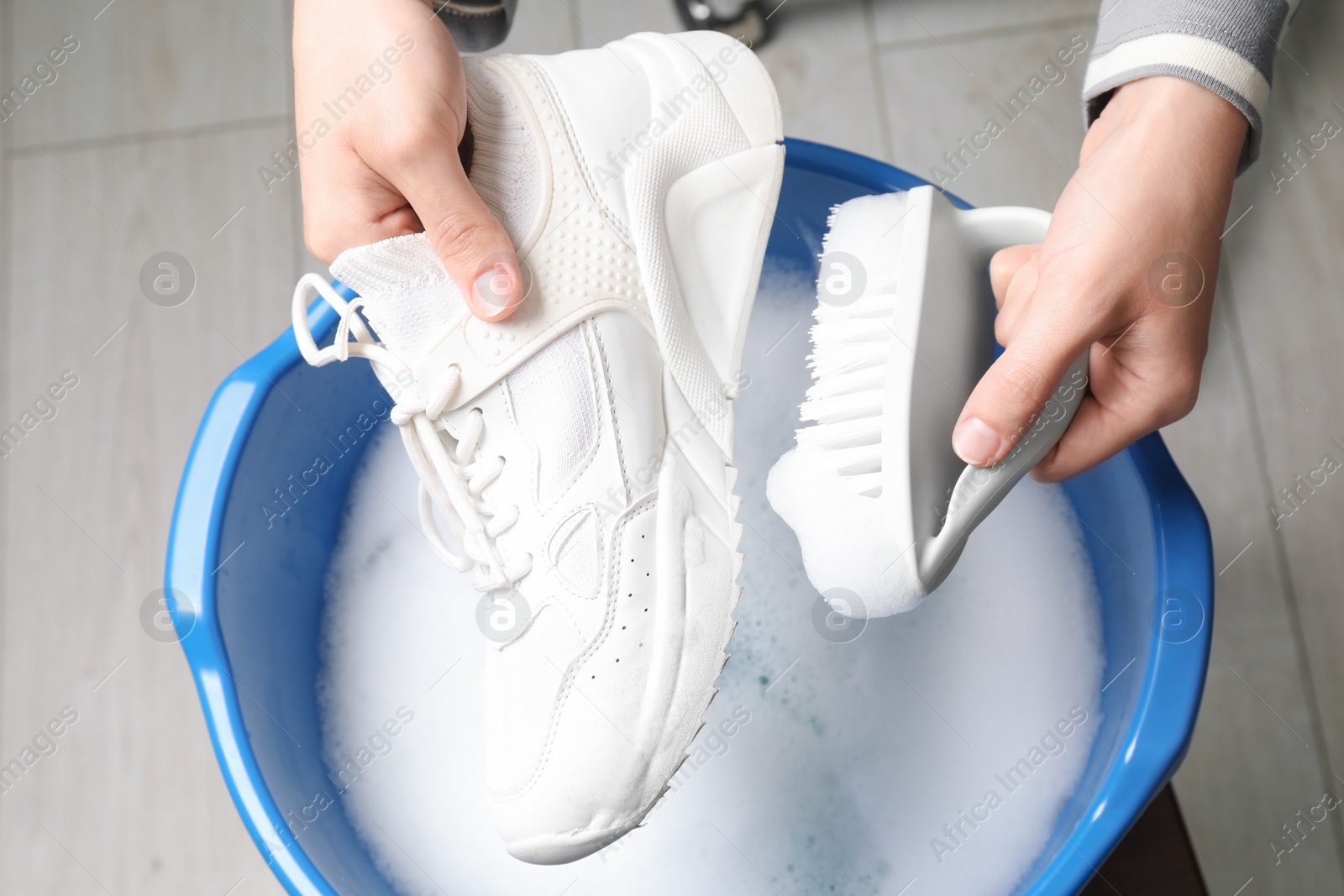 Photo of Woman cleaning stylish sneakers with brush in wash basin, top view