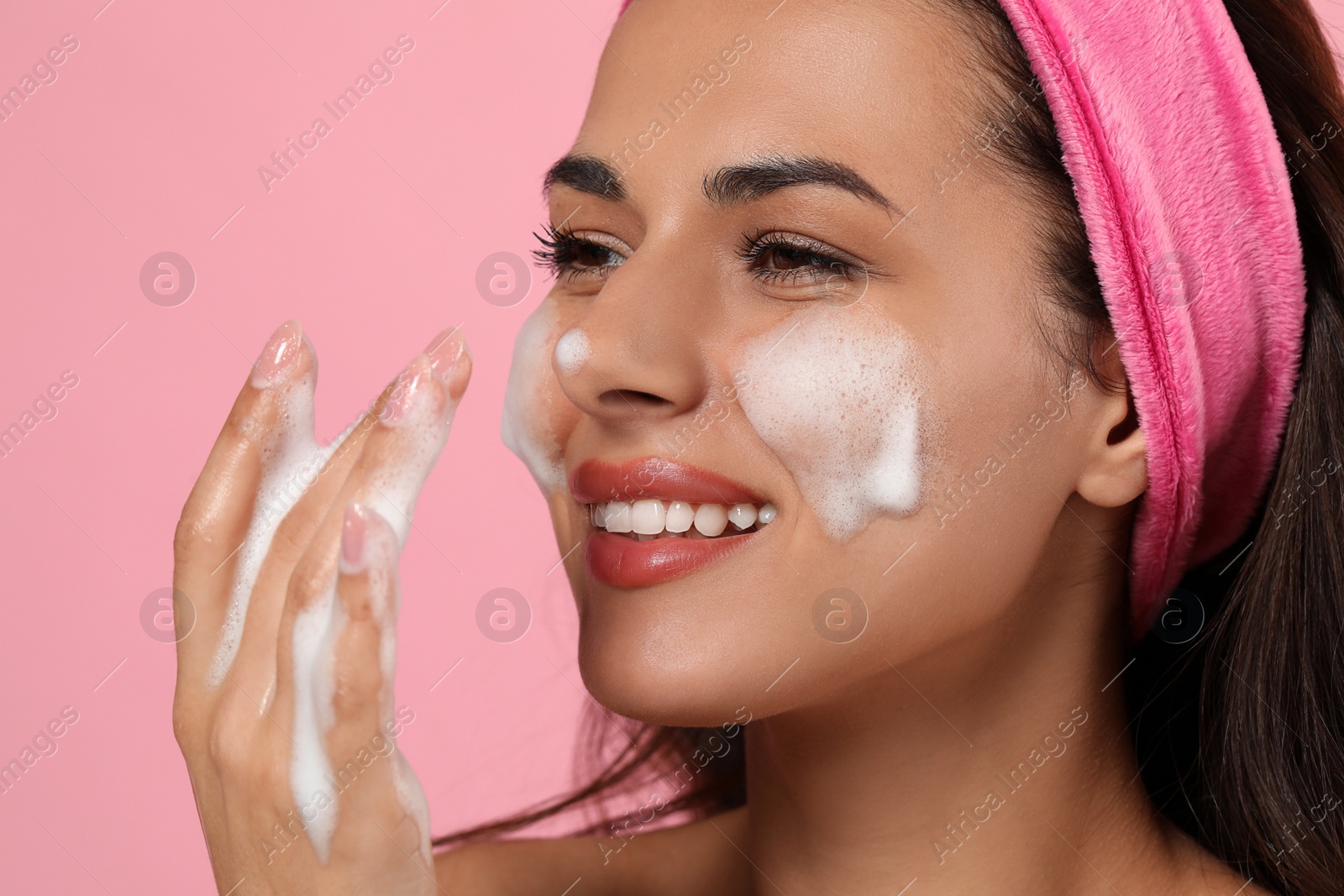 Photo of Beautiful woman applying facial cleansing foam on pink background, closeup