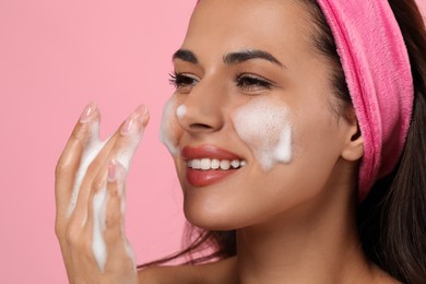 Photo of Beautiful woman applying facial cleansing foam on pink background, closeup