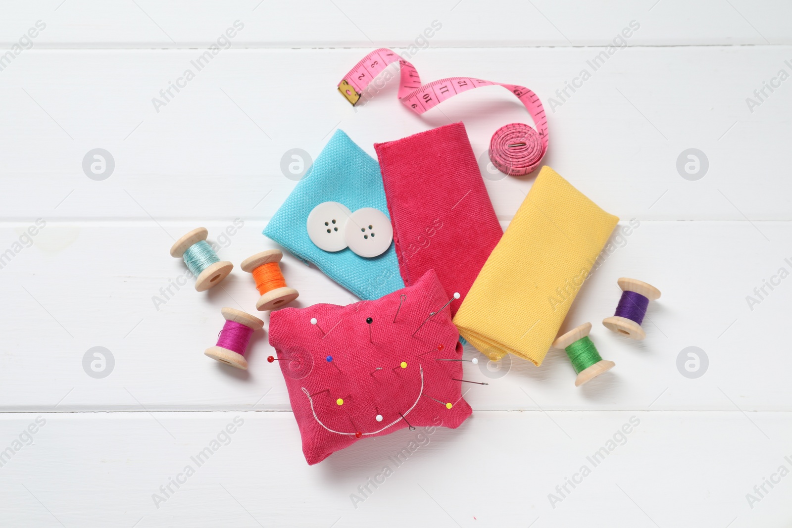 Photo of Red pincushion with pins and other sewing tools on white wooden table, flat lay