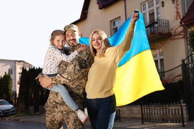 Soldier in military uniform reunited with his family and Ukrainian flag on city street