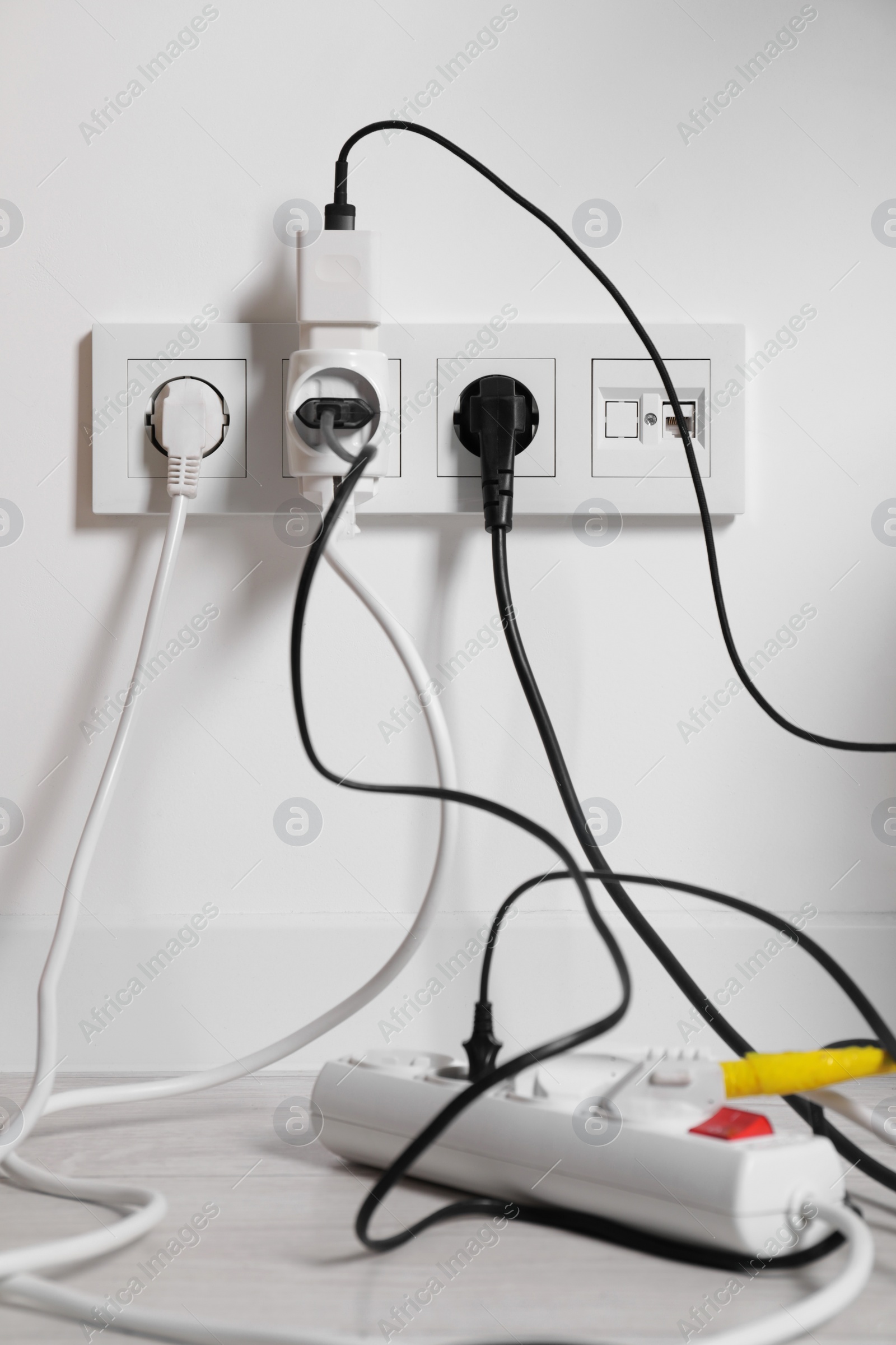 Photo of Different electrical plugs in socket and power strip on floor indoors