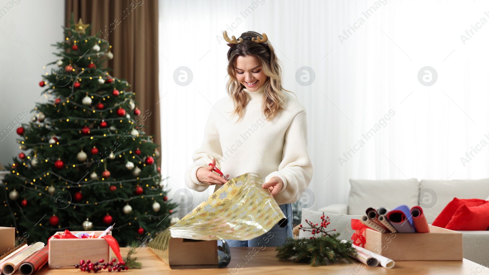 Photo of Beautiful young woman wrapping Christmas gift at home