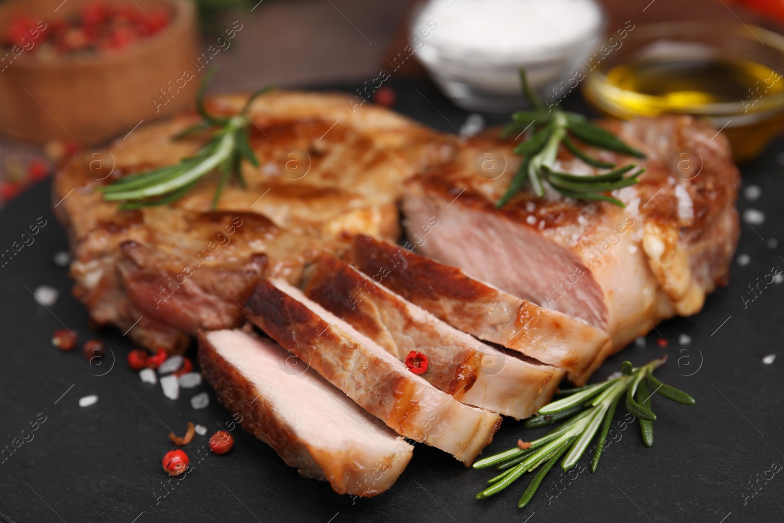 Photo of Pieces of delicious fried meat with rosemary and spices on slate plate, closeup