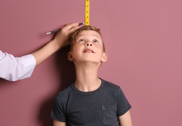 Photo of Doctor measuring little boy's height on color background