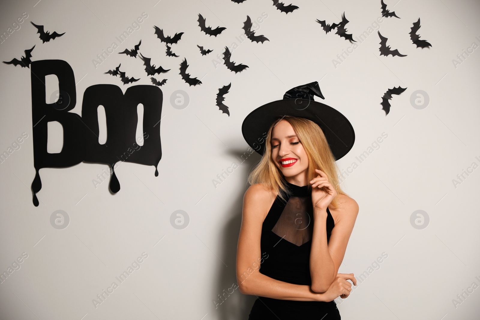 Photo of Woman in witch hat posing near white wall decorated for Halloween