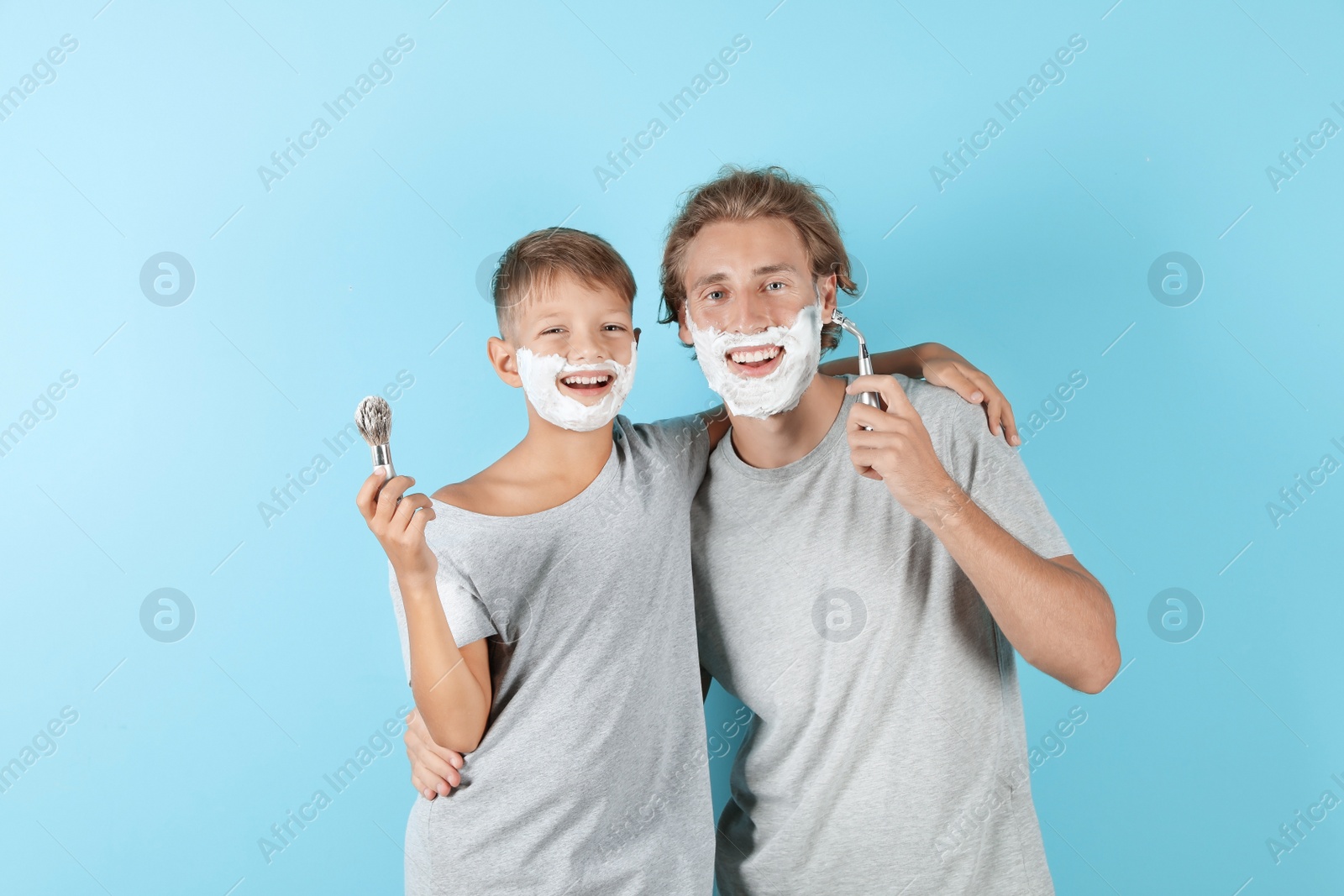 Photo of Father and son shaving together on color background