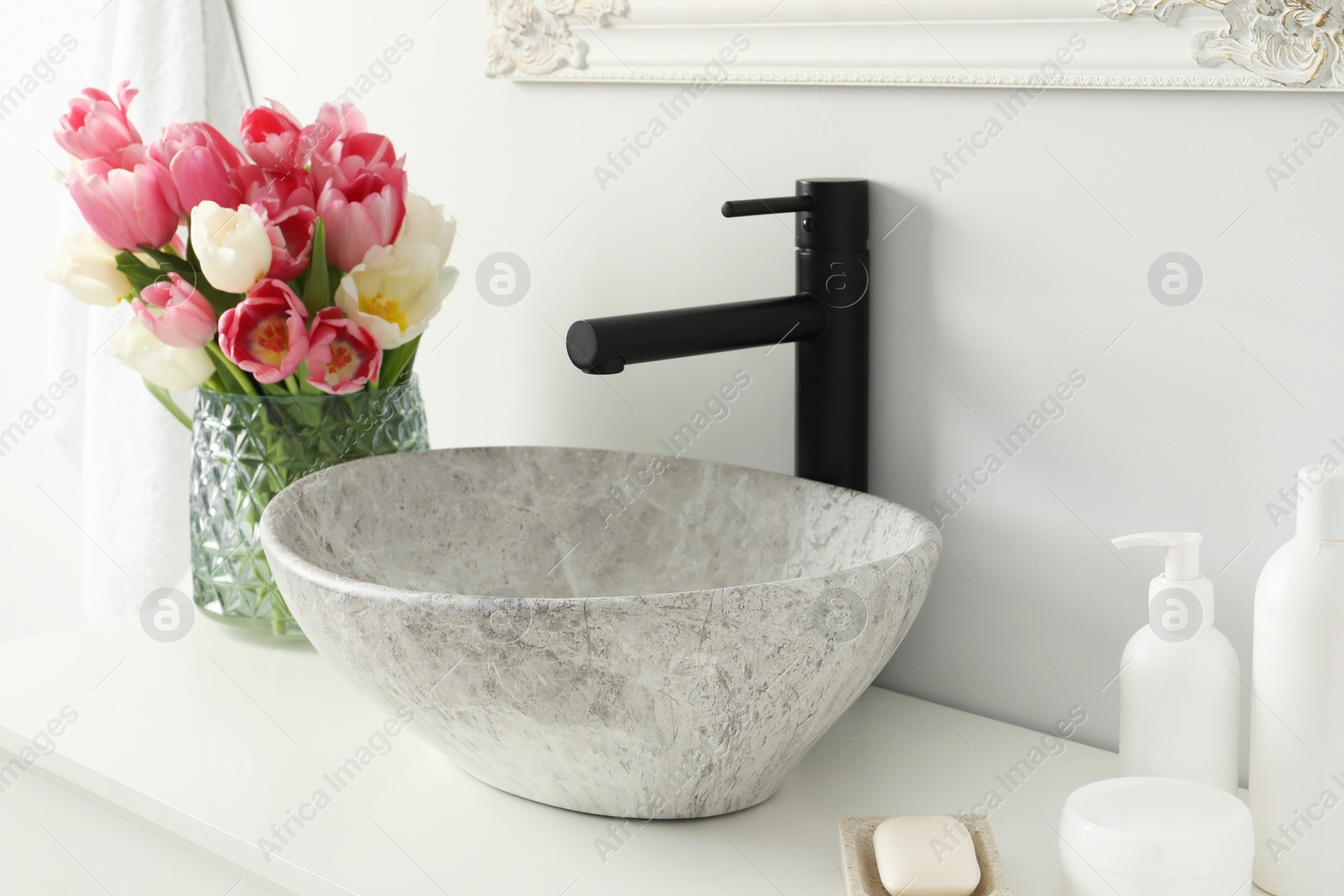 Photo of Vase with beautiful pink tulips and toiletries near sink in bathroom