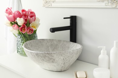 Photo of Vase with beautiful pink tulips and toiletries near sink in bathroom