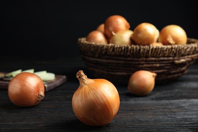 Photo of Ripe onions on black wooden table, space for text