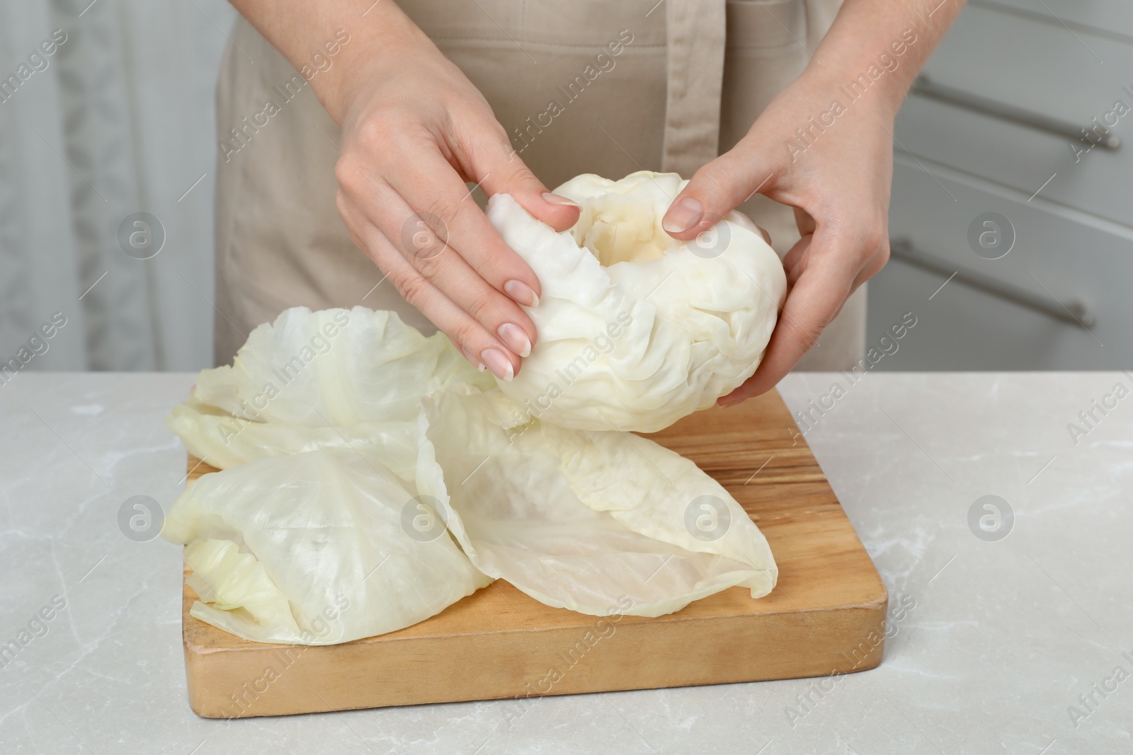 Photo of Woman preparing stuffed cabbage rolls at light grey table, closeup