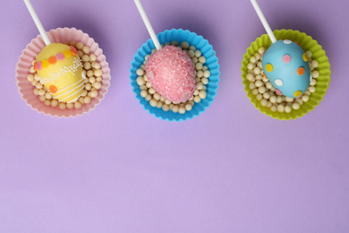 Photo of Egg shaped cake pops and space for text on violet background, flat lay. Easter celebration