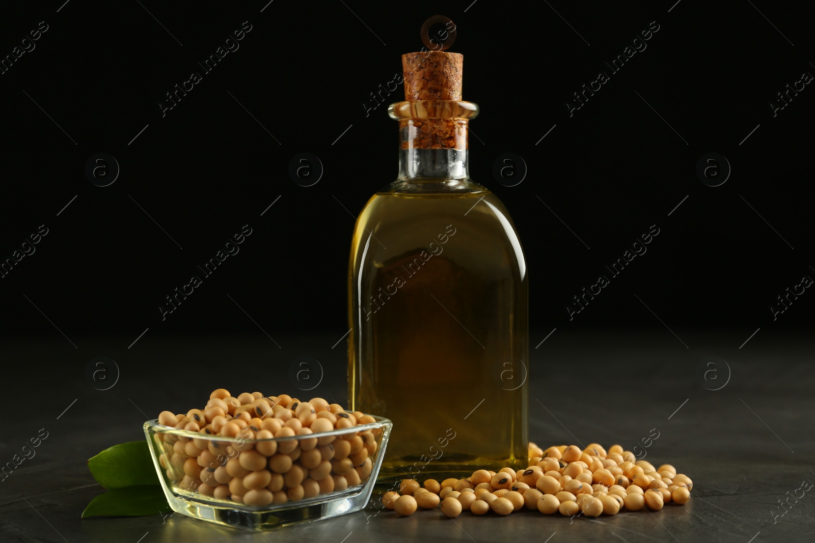 Photo of Glass bottle of oil, leaves and soybeans on grey table