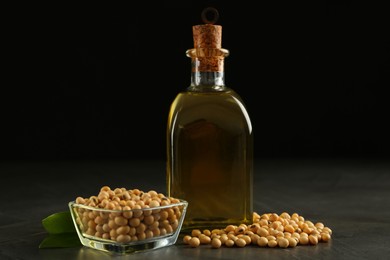 Photo of Glass bottle of oil, leaves and soybeans on grey table