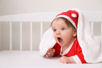 Cute baby wearing festive Christmas costume in crib. Space for text