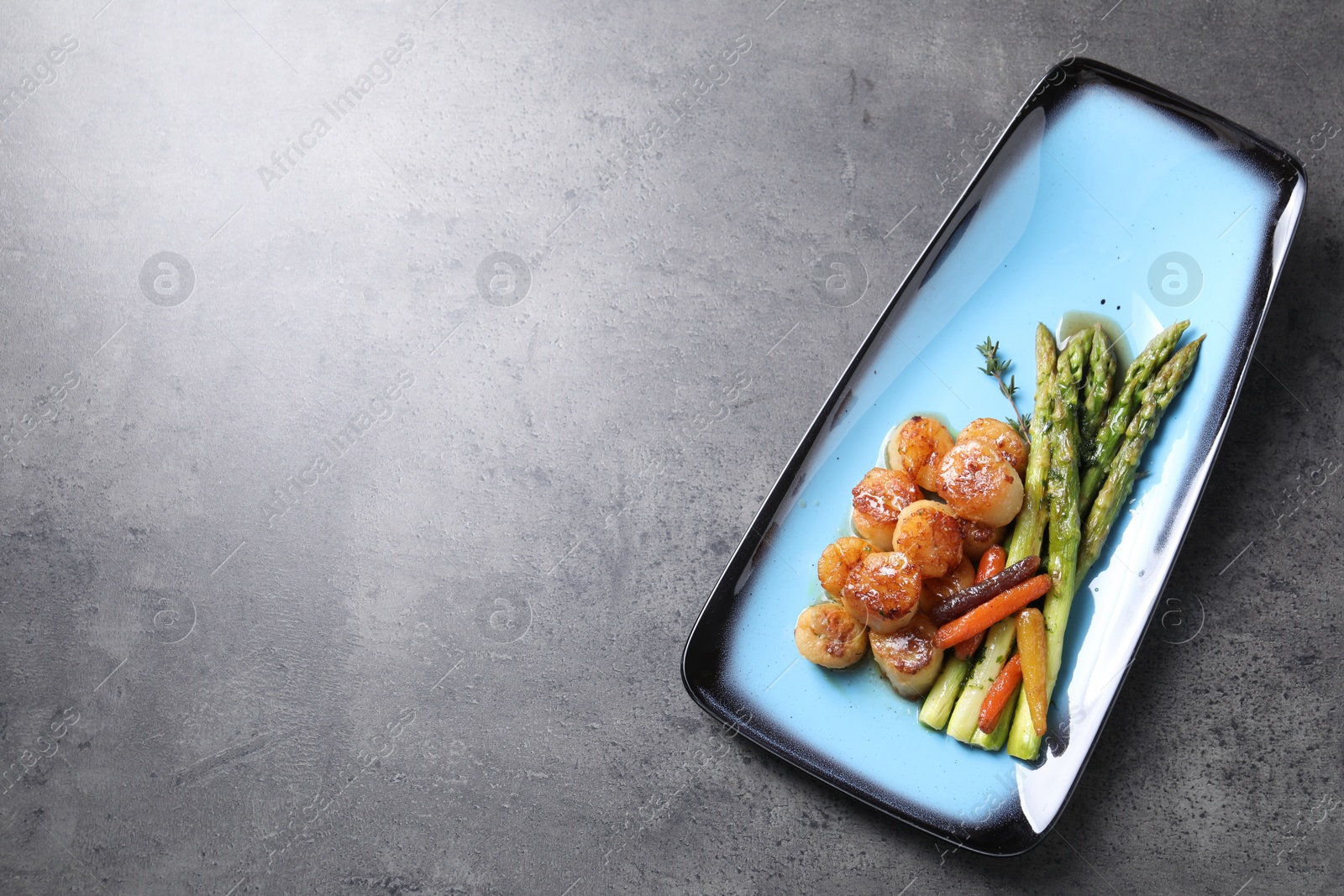 Photo of Delicious fried scallops with asparagus and vegetables on grey table, top view. Space for text