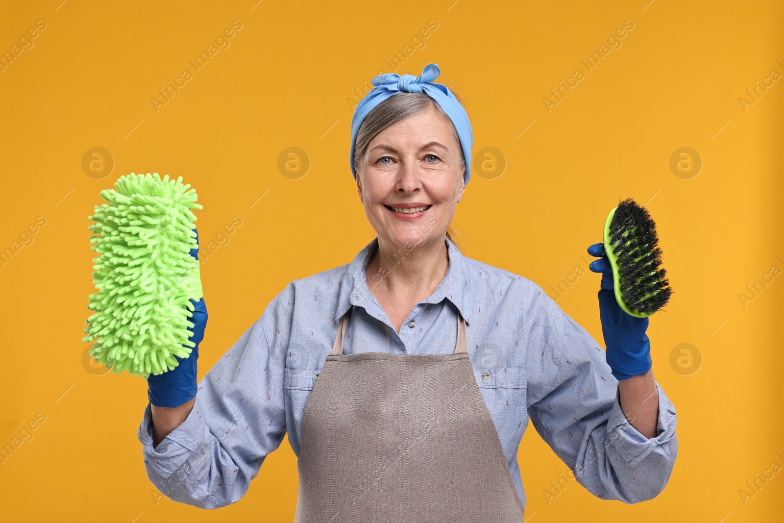 Photo of Happy housewife with rag and brush on orange background