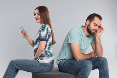 Photo of Woman with smartphone ignoring her boyfriend on light grey background. Relationship problems
