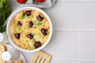 Photo of Tasty sausage casserole with green onions in baking dish served on white tiled table, flat lay. Space for text