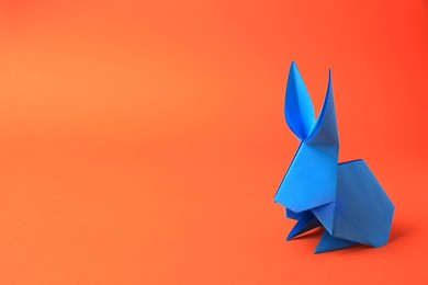 Photo of Origami art. Beautiful paper rabbit on orange background, space for text