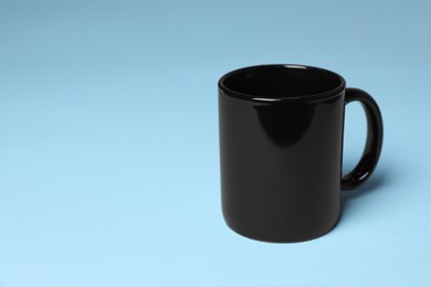 Photo of One black ceramic mug on light blue background, space for text