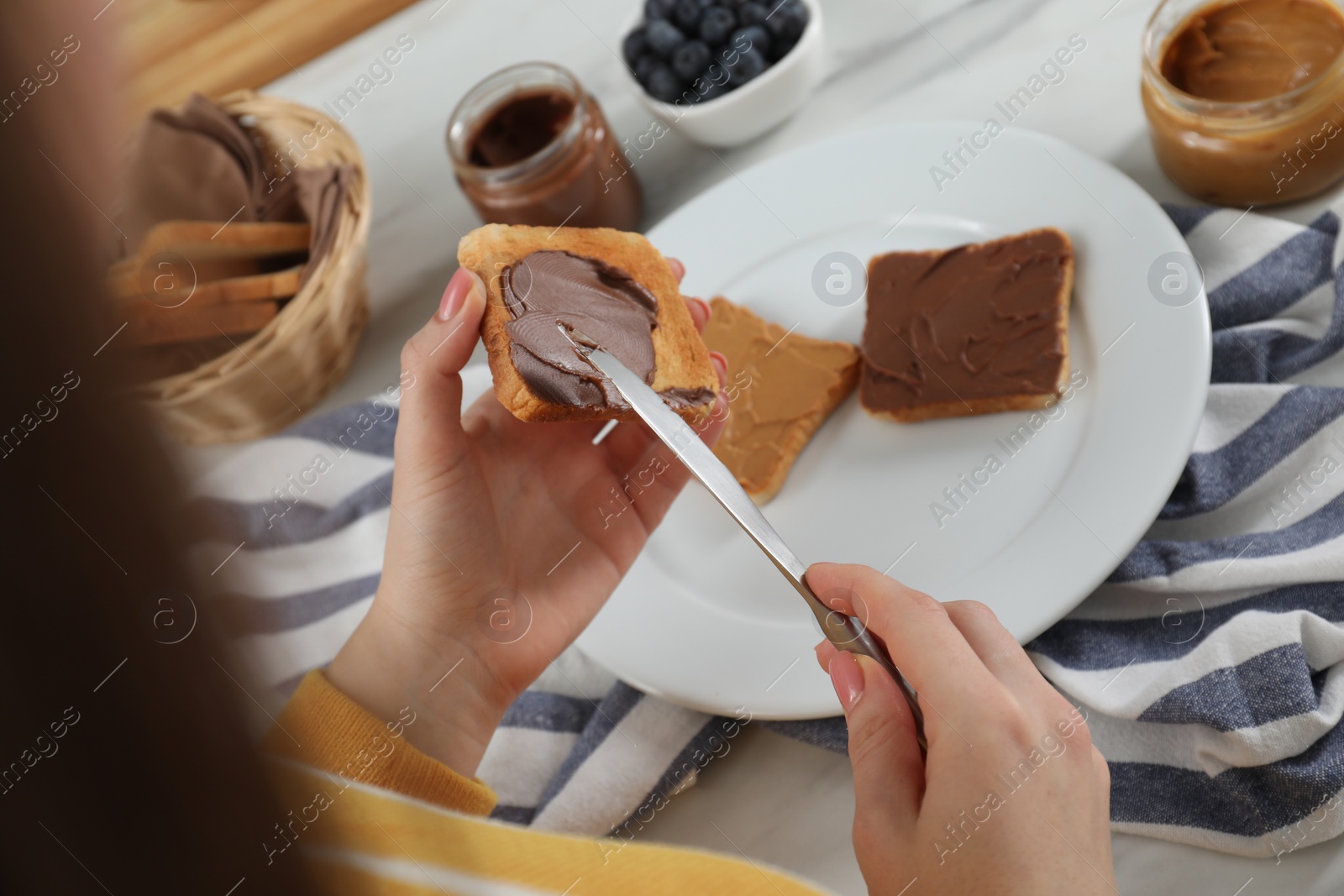 Photo of Woman spreading tasty nut butter onto toast at table, closeup