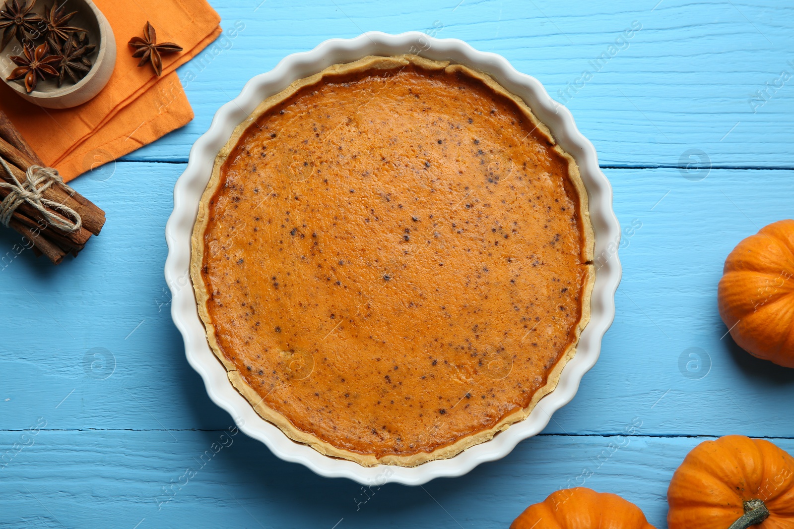Photo of Delicious pumpkin pie and ingredients on light blue wooden table, flat lay