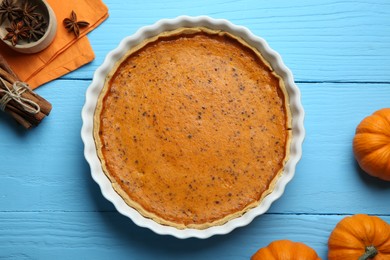 Delicious pumpkin pie and ingredients on light blue wooden table, flat lay