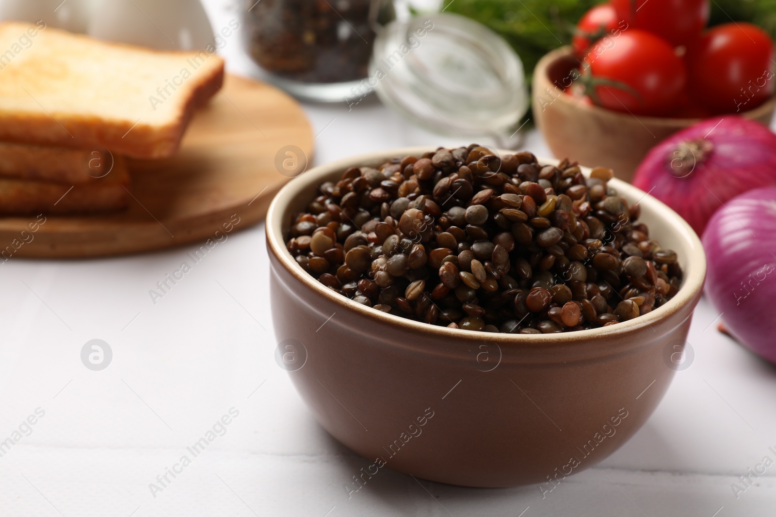 Photo of Delicious lentils in bowl served on white table, closeup. Space for text