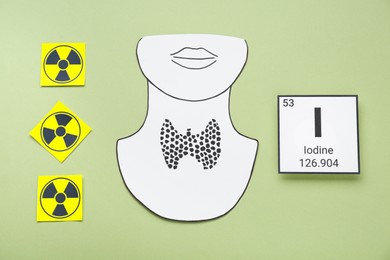 Photo of Card with chemical element Iodine, paper cutout of thyroid gland and radiation signs on olive background, flat lay