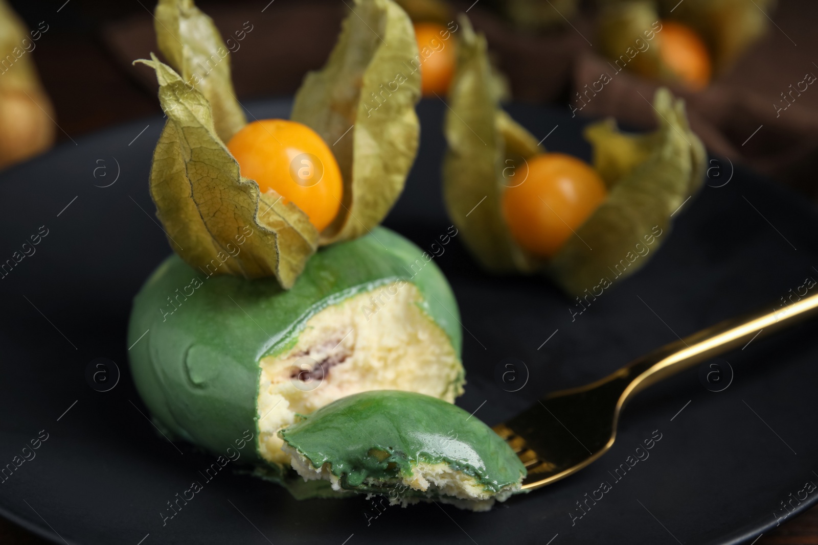 Photo of Delicious mousse cake decorated with physalis fruit on black plate, closeup