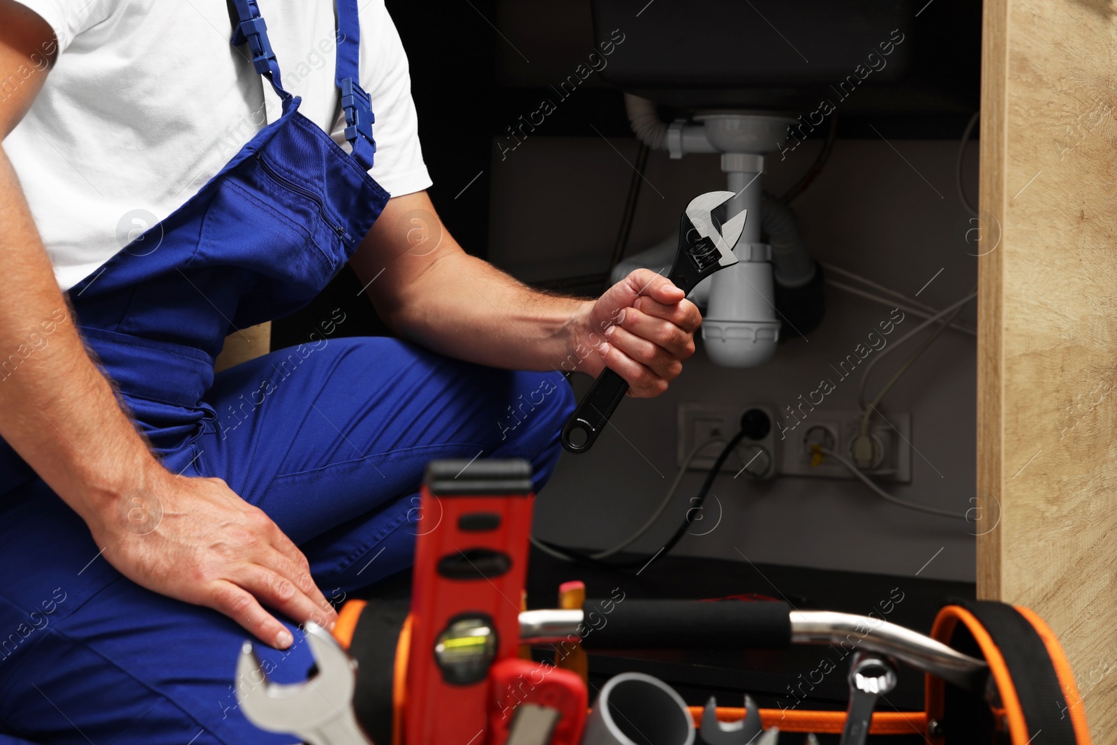 Photo of Professional plumber with adjustable wrench under kitchen sink, closeup