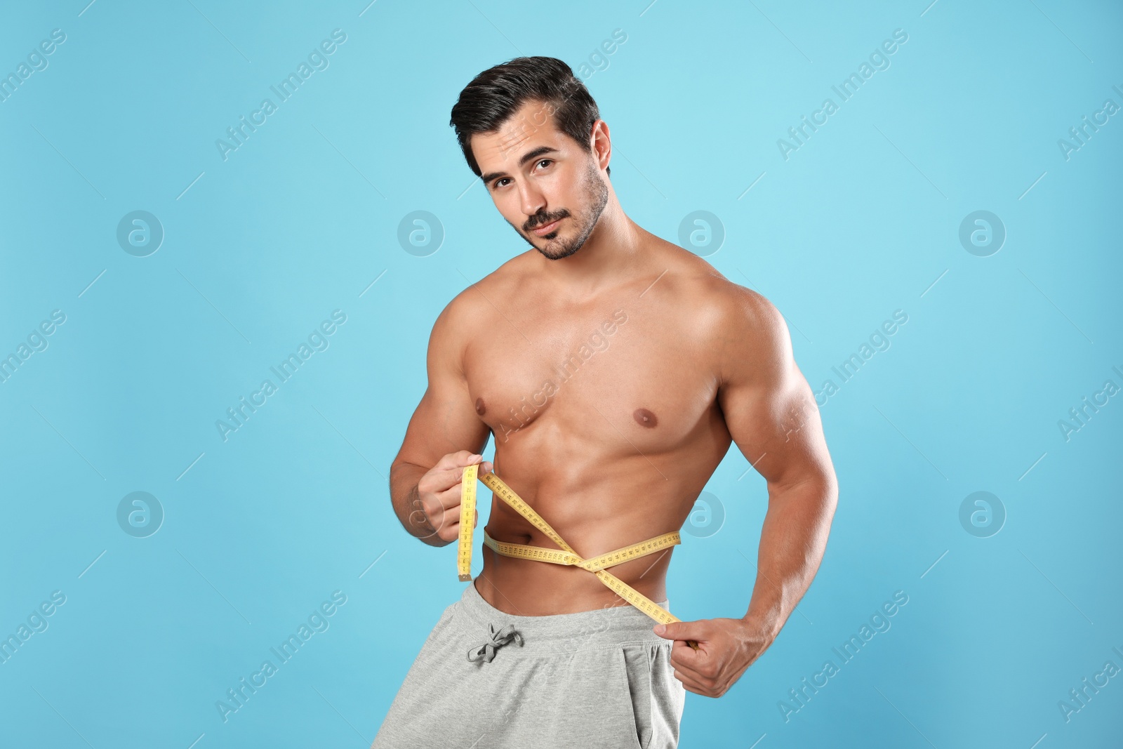 Photo of Young man with slim body using measuring tape on light blue background