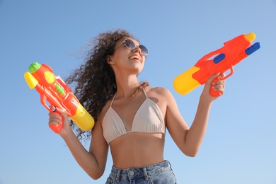 Photo of African American woman with water guns against blue sky, low angle view