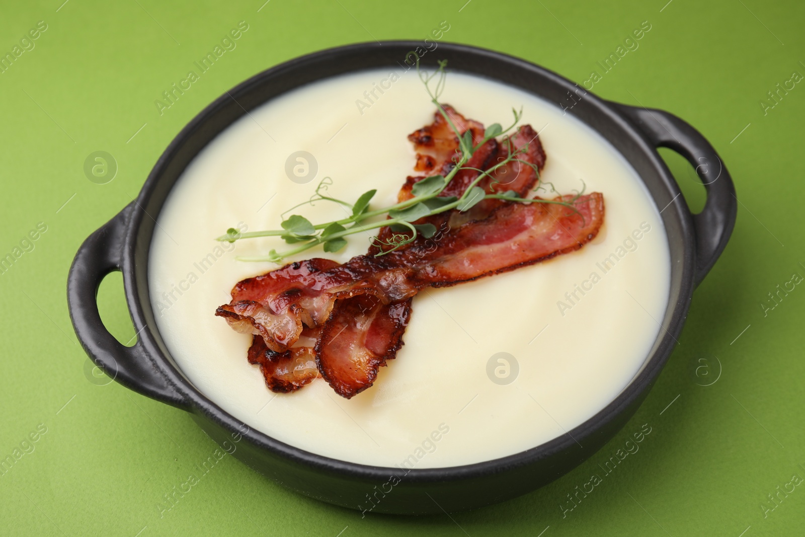 Photo of Delicious potato soup with bacon and microgreens in bowl on green table, closeup