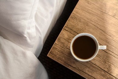 Photo of Cup of morning coffee on wooden night stand near bed, top view