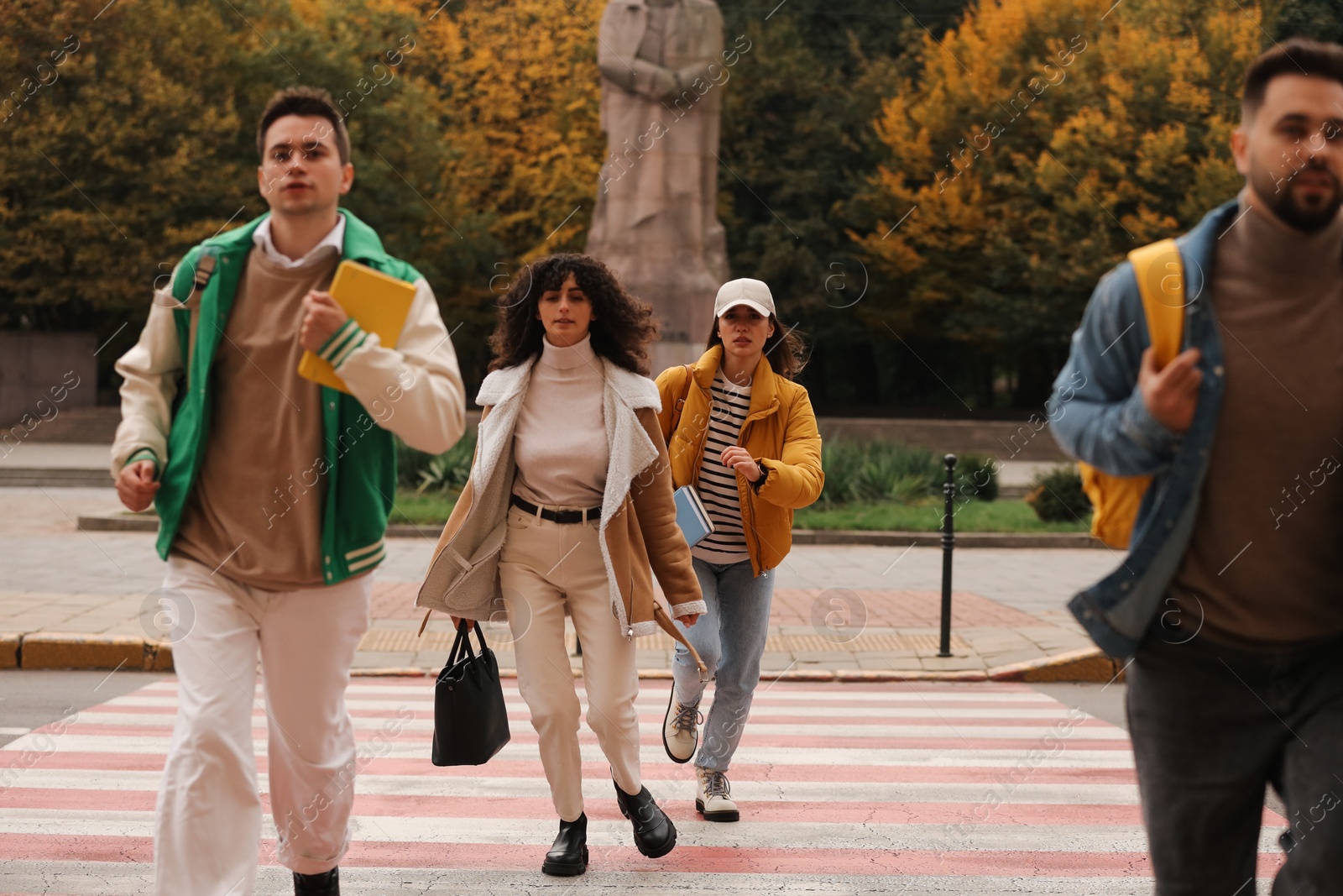 Photo of Being late. Group of students running on pedestrian crossing outdoors