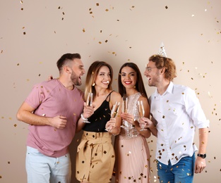 Happy friends with champagne in glasses and confetti on color background