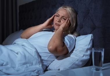 Photo of Mature woman suffering from headache in bed at night