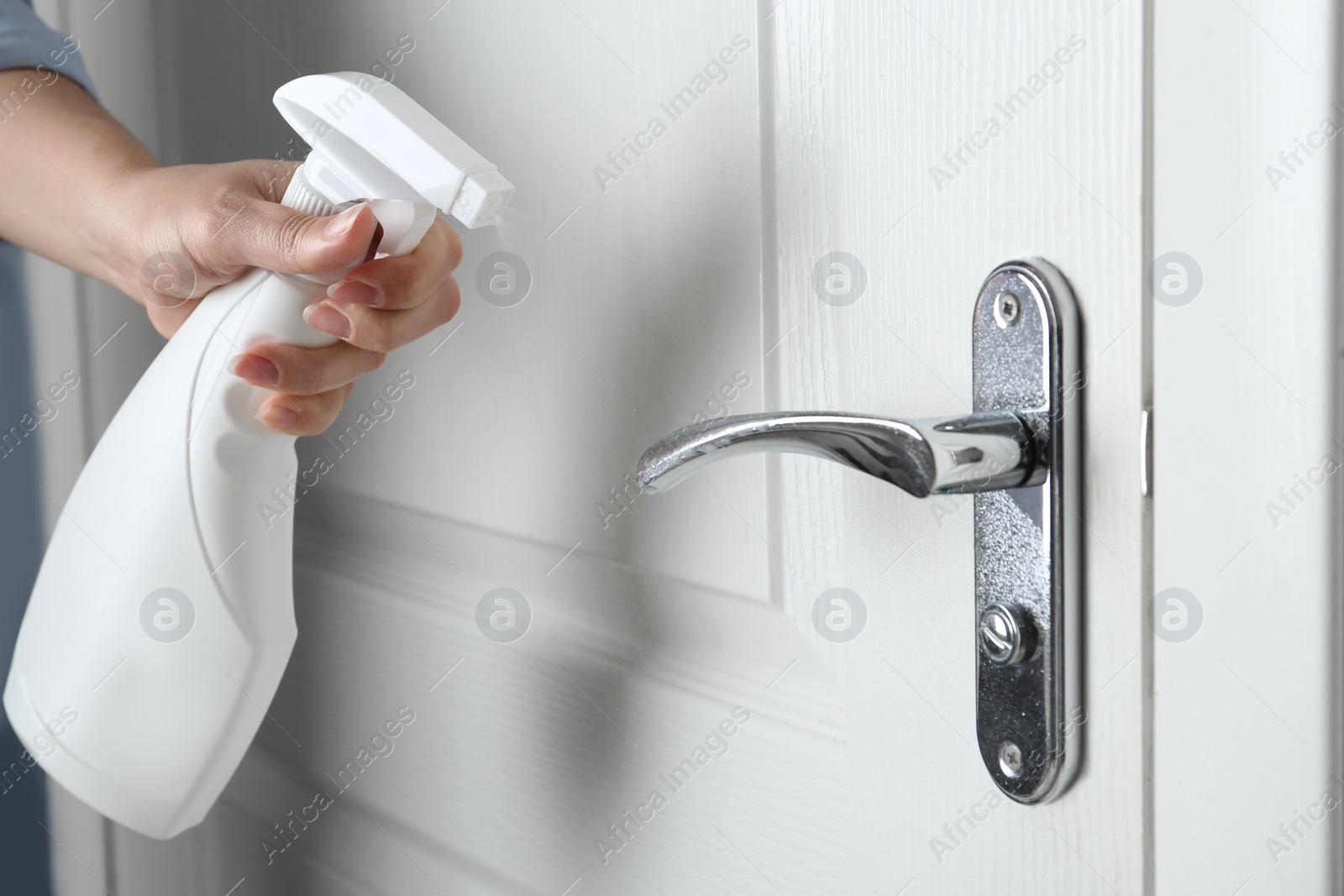 Photo of Woman spraying antiseptic onto door handle indoors, closeup