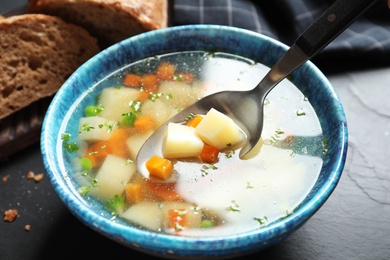 Spoon of fresh homemade vegetable soup over full bowl on black table, closeup