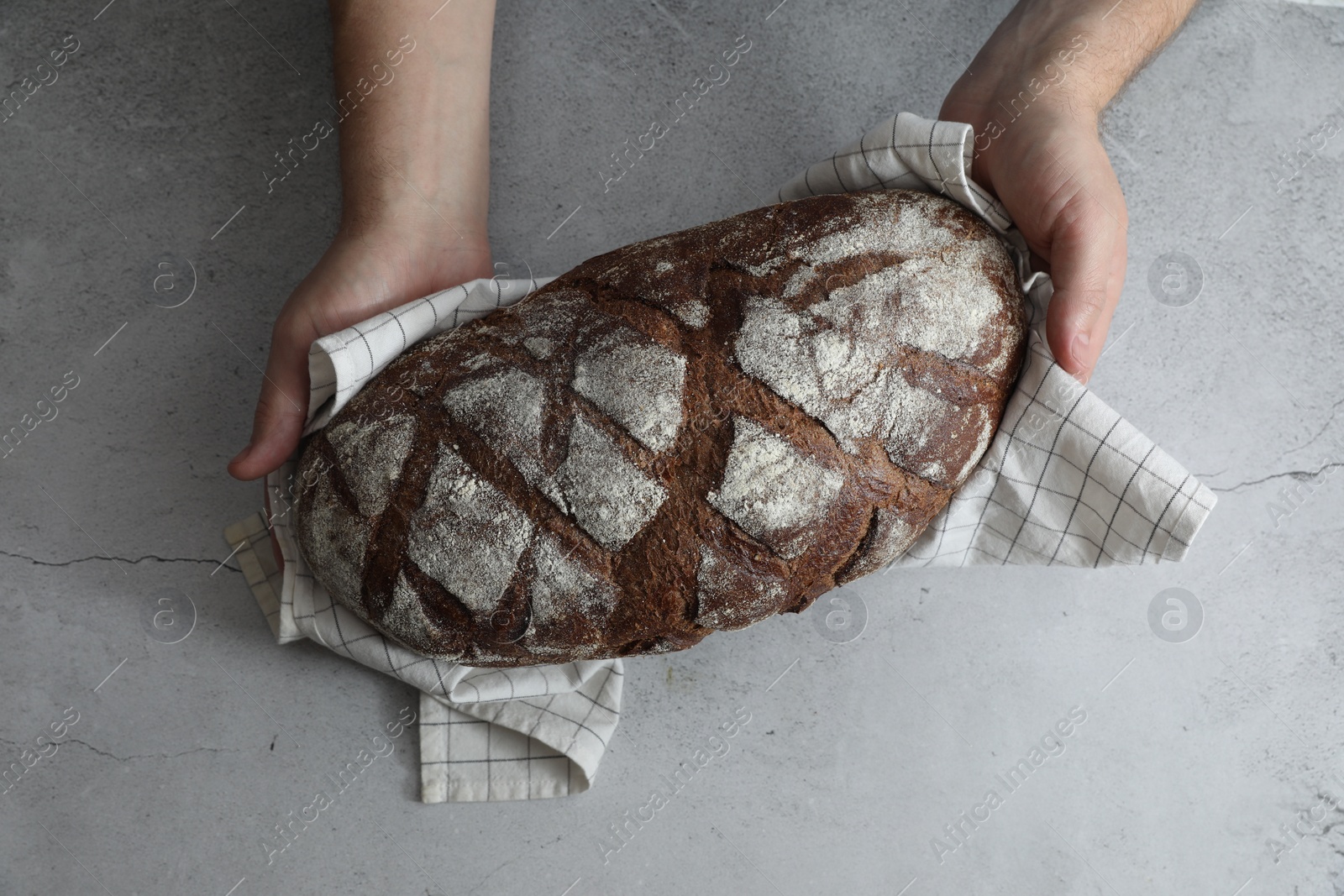 Photo of Man holding loaf of fresh bread at grey table, top view