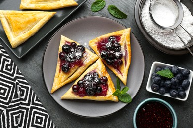 Photo of Fresh tasty puff pastry with sugar powder, jam, sweet berries and mint served on grey table, flat lay