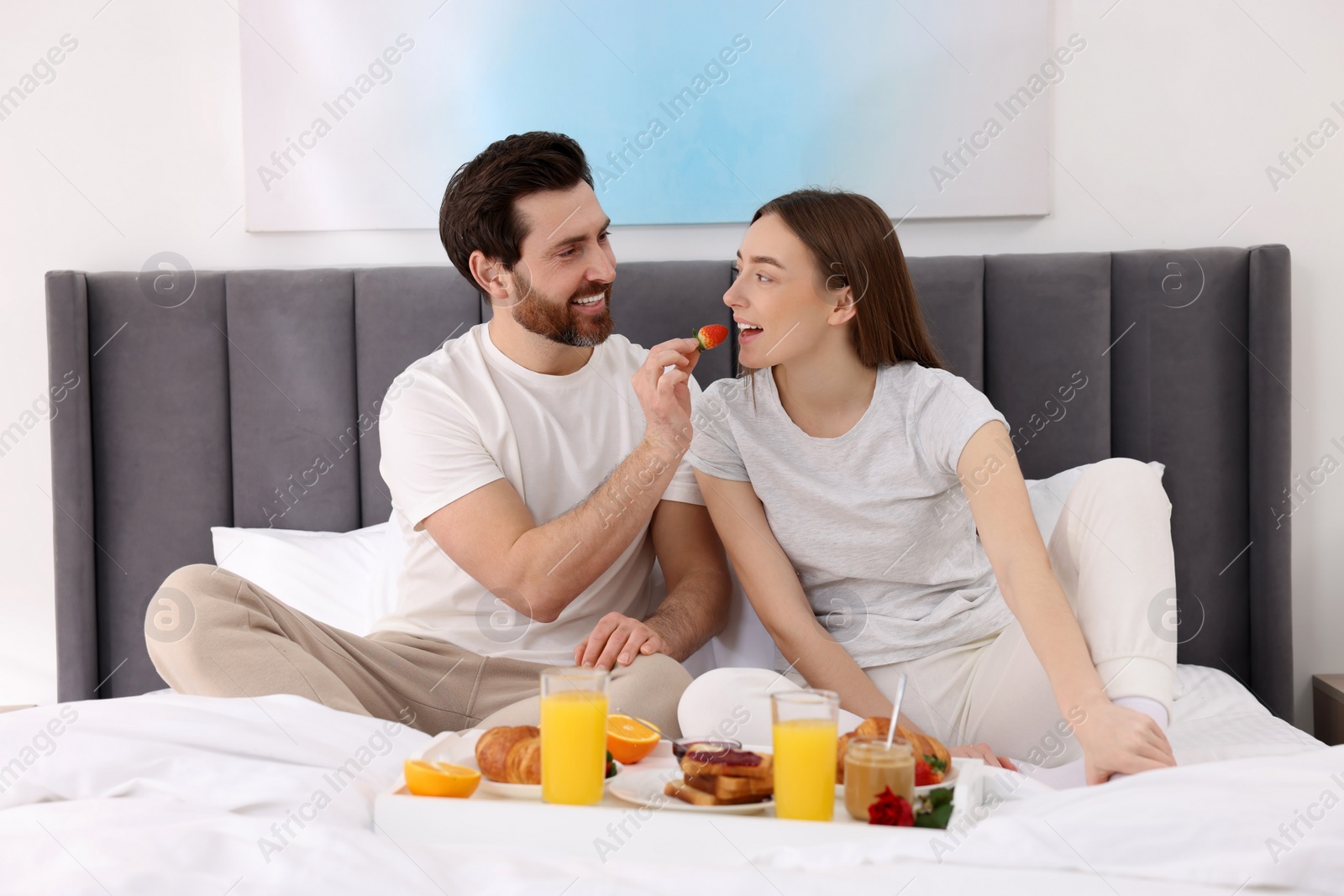 Photo of Healthy breakfast. Happy husband feeding his wife on bed at home