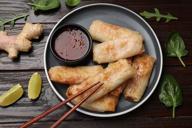 Photo of Tasty fried spring rolls, lime, sauce and other products on wooden table, flat lay