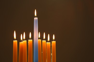 Photo of Hanukkah celebration. Burning candles on brown background, space for text