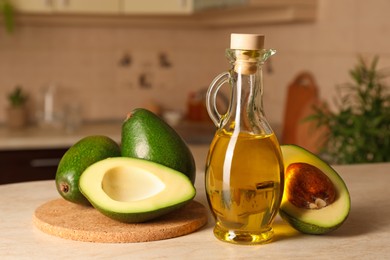 Fresh avocados and jug of cooking oil on beige marble table in kitchen